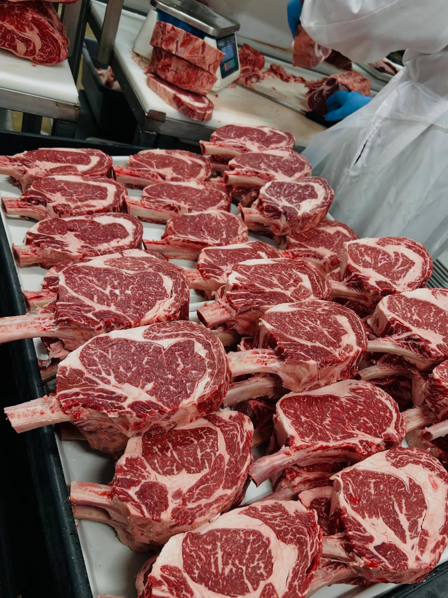 Trays of thick bone-in ribeye steaks being cut and weighed